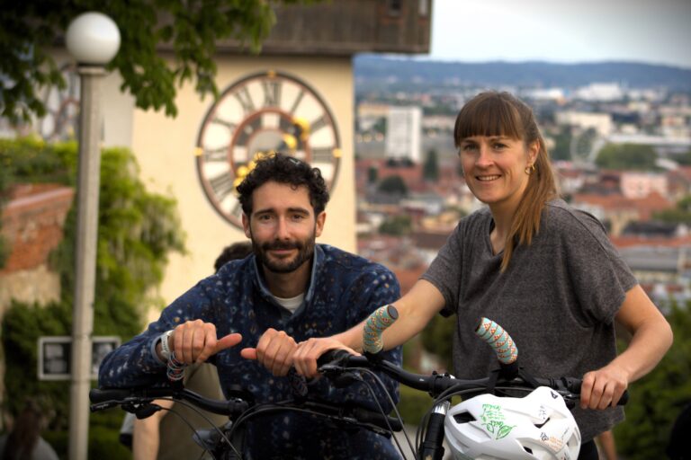 two person on bikes in front of clocktower graz